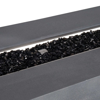 Detailed close-up of the Flame Havens Refuge Series 68 x 30 x 24-inch gray GFRC concrete propane fire pit, showing glossy black reflective fire glass spread across the linear stainless steel burner pan with the perforated ignition cage visible near the center.