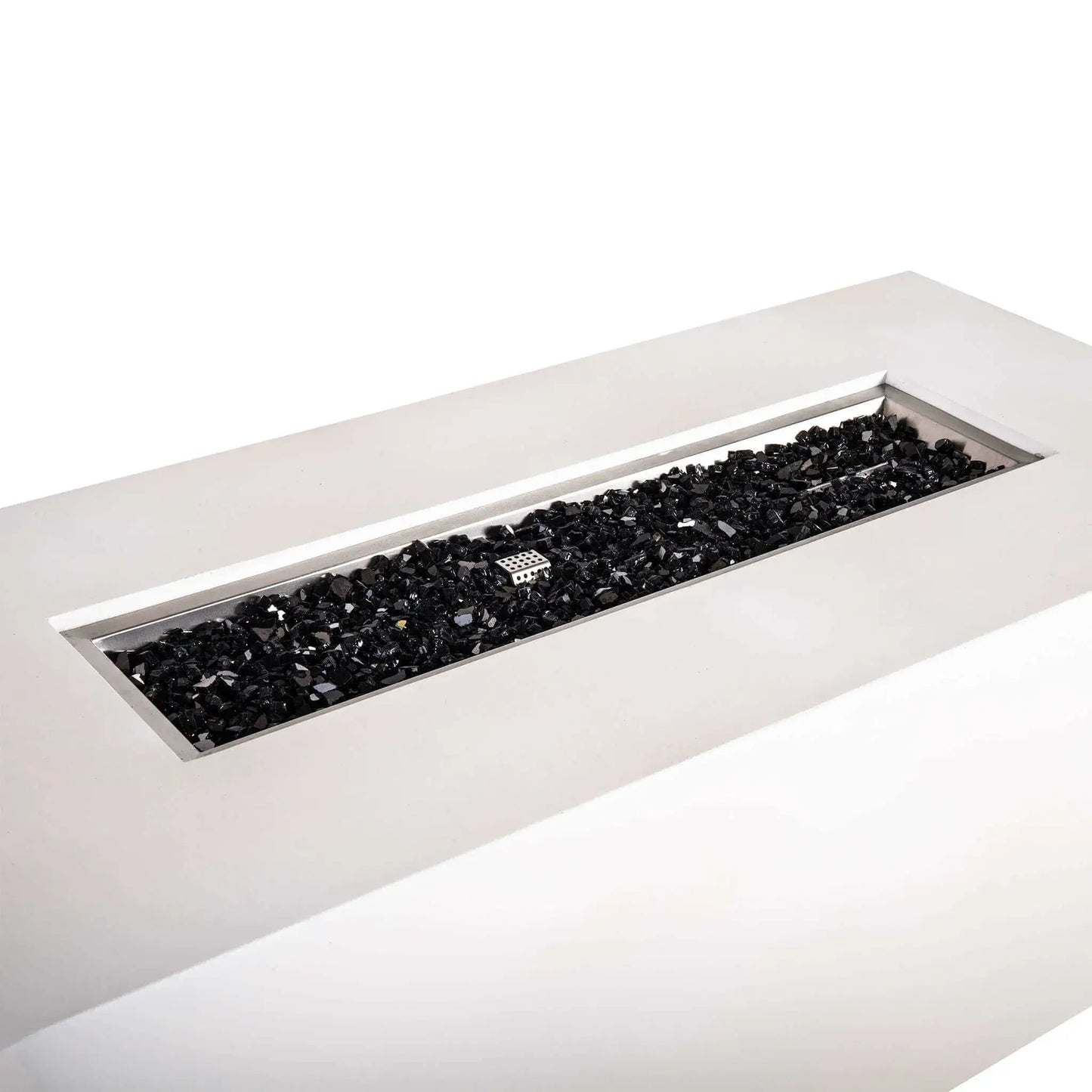 Angled close-up of the Flame Havens Refuge Series 68 x 30 x 24-inch rectangular propane gas fire pit in white GFRC concrete, showing the long stainless steel burner pan filled with reflective black fire glass and the protective ignition cage centered among the glass.