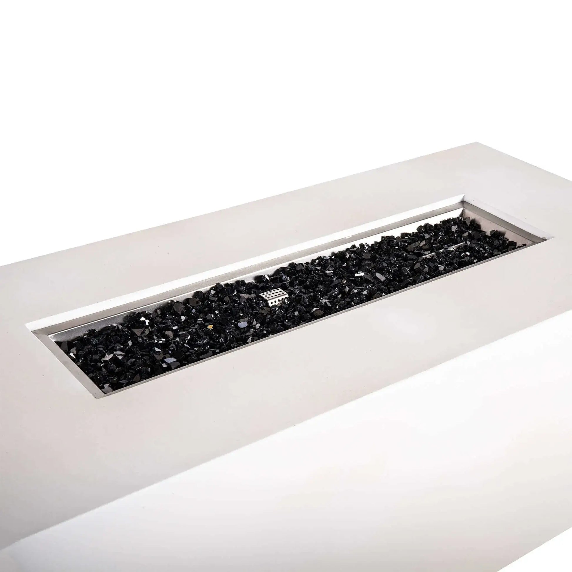 Angled close-up of the Flame Havens Refuge Series 68 x 30 x 24-inch rectangular propane gas fire pit in white GFRC concrete, showing the long stainless steel burner pan filled with reflective black fire glass and the protective ignition cage centered among the glass.