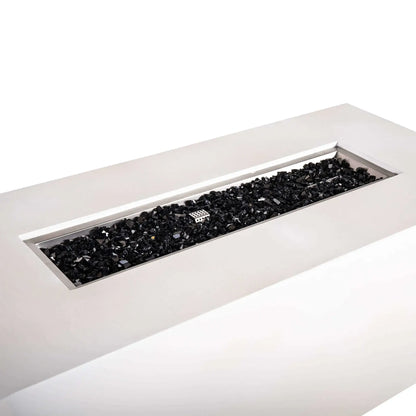 Angled close-up of the Flame Havens Refuge Series 68 x 30 x 24-inch rectangular propane gas fire pit in white GFRC concrete, showing the long stainless steel burner pan filled with reflective black fire glass and the protective ignition cage centered among the glass.