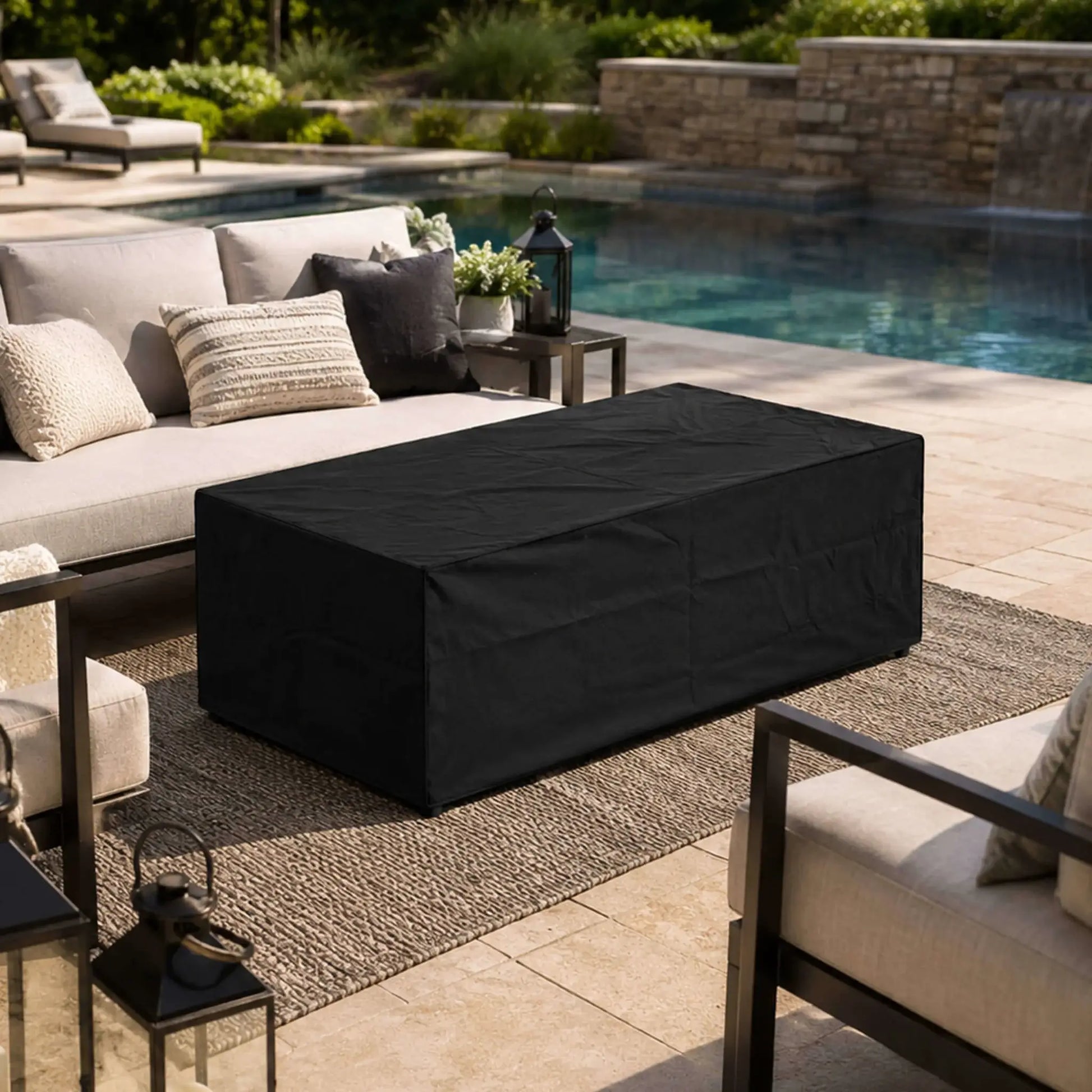 Flame Havens Refuge Series 68 x 30 x 24-inch rectangular propane fire pit protected by a fitted black canvas fabric cover on an outdoor poolside patio. The covered fire pit is surrounded by cushioned lounge seating, decorative lanterns, a textured rug, landscaping, and a stone waterfall.
