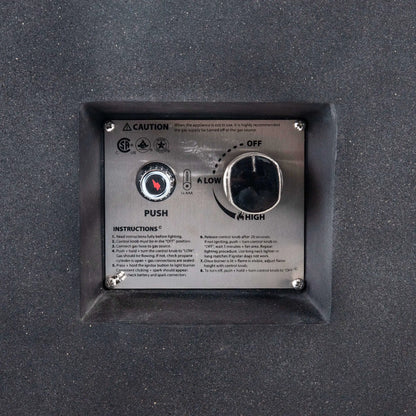 Close-up of the recessed CSA ignition controls on the Flame Havens Refuge Series 68 x 30 x 24-inch black GFRC concrete propane fire pit. The stainless steel panel shows a push-button spark ignitor, AAA battery indicator, adjustable control knob with off, low, and high settings, safety certifications, and operating instructions.