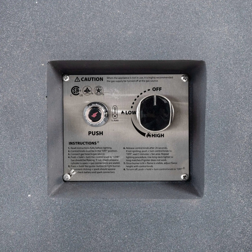 Close-up of the recessed CSA ignition controls on the Flame Havens Refuge Series gray propane gas fire pit, showing the push-button spark igniter, adjustable control knob with OFF, LOW, and HIGH settings, operating instructions, and safety markings on a stainless steel panel.