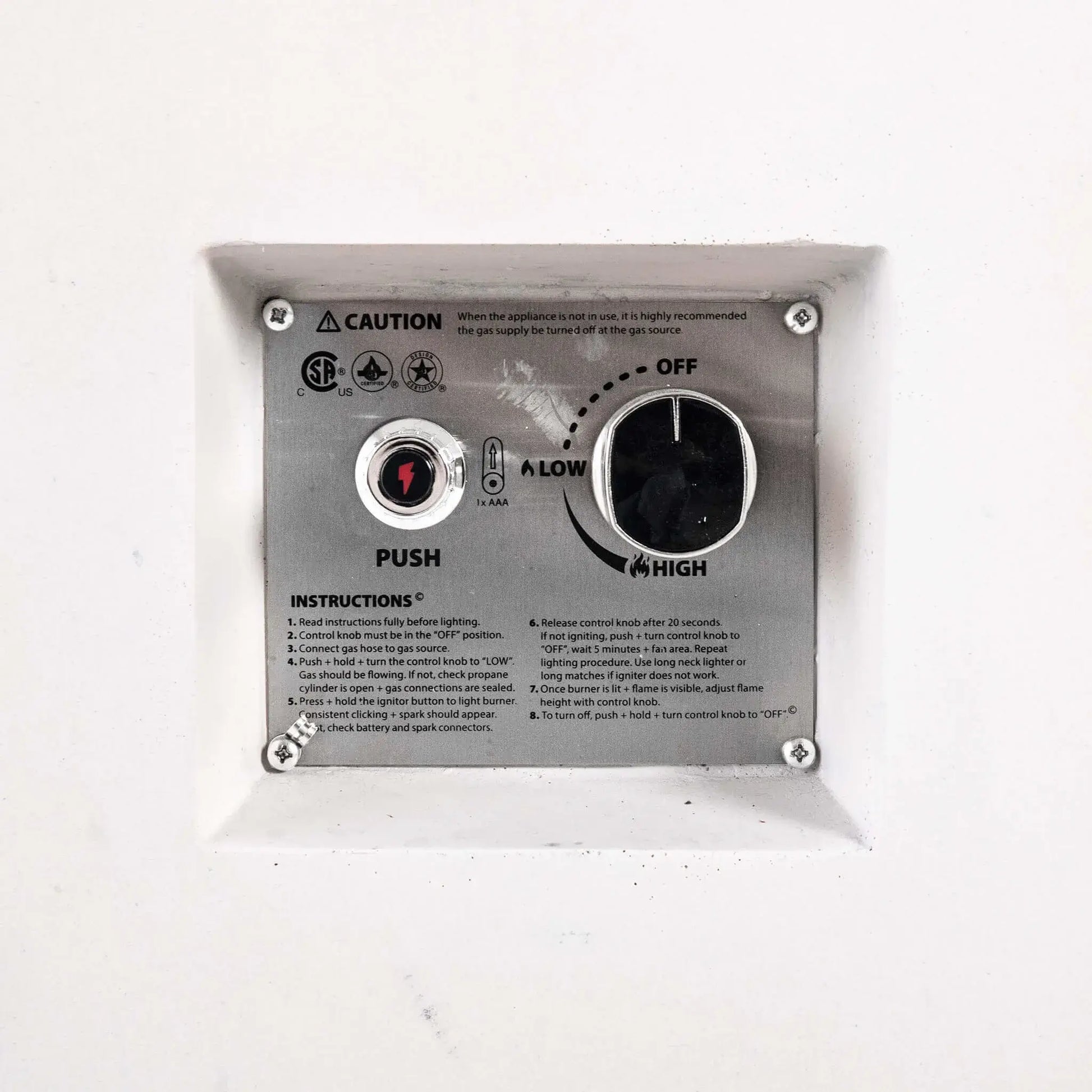 Close-up of the recessed CSA ignition controls on the Flame Havens Refuge Series 68 x 30 x 24-inch white rectangular propane fire pit. The stainless steel panel includes a push-button battery ignitor, large flame control knob with off, low, and high settings, safety certifications, caution notice, and lighting instructions.