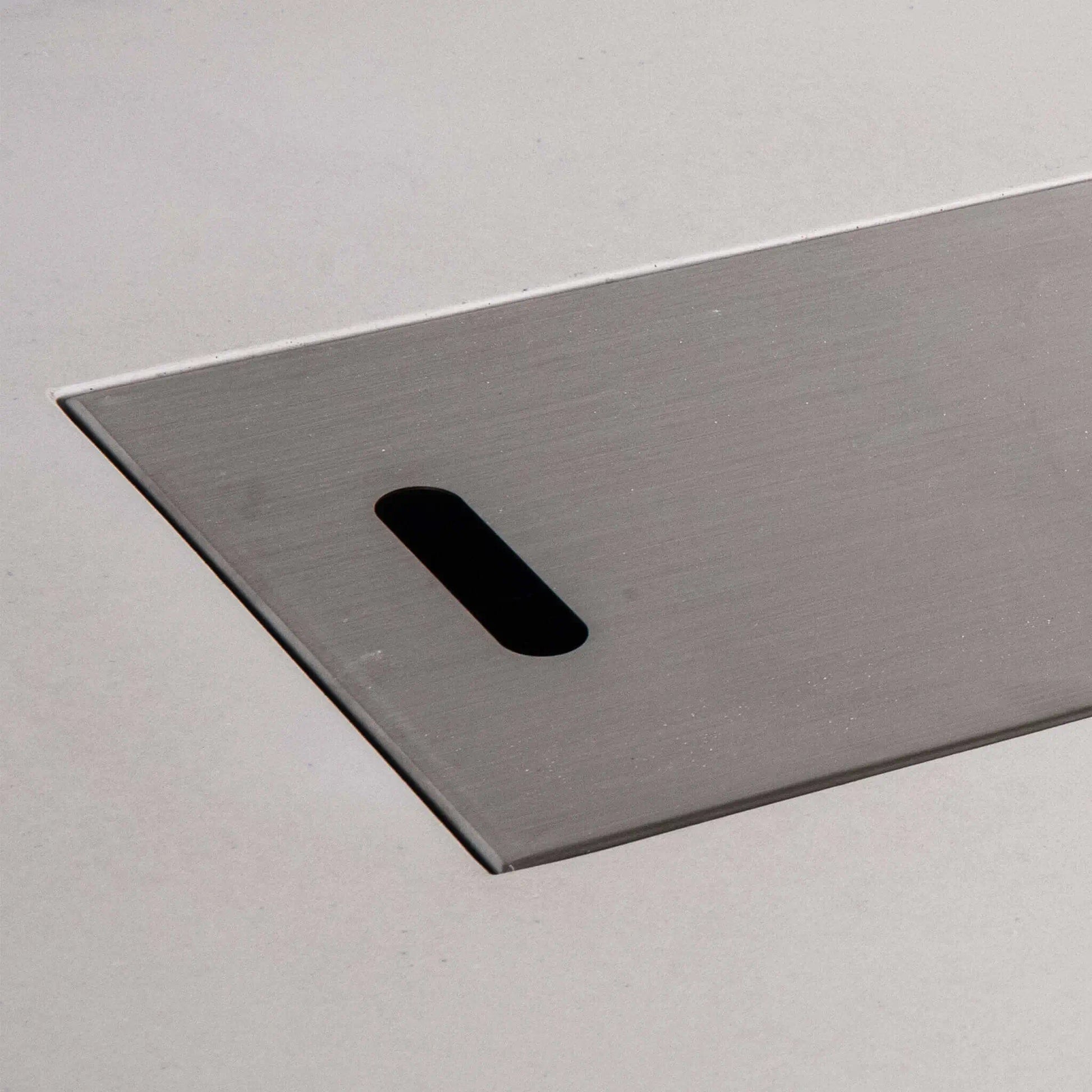 Close-up of the brushed stainless steel burner cover for the Flame Havens Refuge Series 68 x 30 x 24-inch rectangular propane fire pit. The image highlights the smooth metal finish, clean beveled edge, and elongated hand slot used to lift the cover from the white GFRC concrete fire pit.