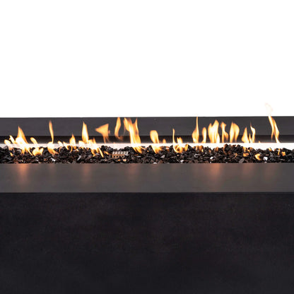 Close-up of bright orange flames burning across reflective tempered black fire glass in the Flame Havens Refuge Series 68 x 30 x 24-inch rectangular black GFRC concrete propane fire pit. The linear flame pattern, stainless steel burner pan, and protective ignition cage are visible against a clean white background.