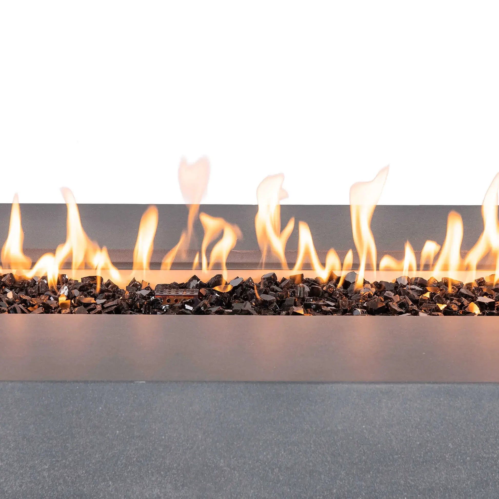 Close-up of bright flames rising across reflective tempered black fire glass in the Flame Havens Refuge Series 68 x 30 x 24-inch rectangular gray propane gas fire pit, with the stainless steel burner pan and ignition cage visible among the glass media.