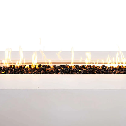 Close-up of the Flame Havens Refuge Series 68 x 30 x 24-inch rectangular propane gas fire pit in white GFRC concrete. A continuous row of bright flames rises above reflective tempered black fire glass, with the protective stainless steel ignition cage visible near the center of the burner.