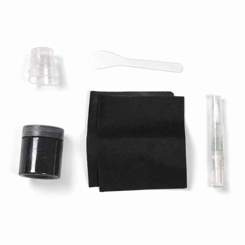 Contents of the Flame Havens Refuge Series Black concrete surface care kit arranged on a white background. The color-matched repair set includes a jar of black material, two black application pads, small clear mixing cups, a plastic mixing spoon, and a clear pen-style applicator.