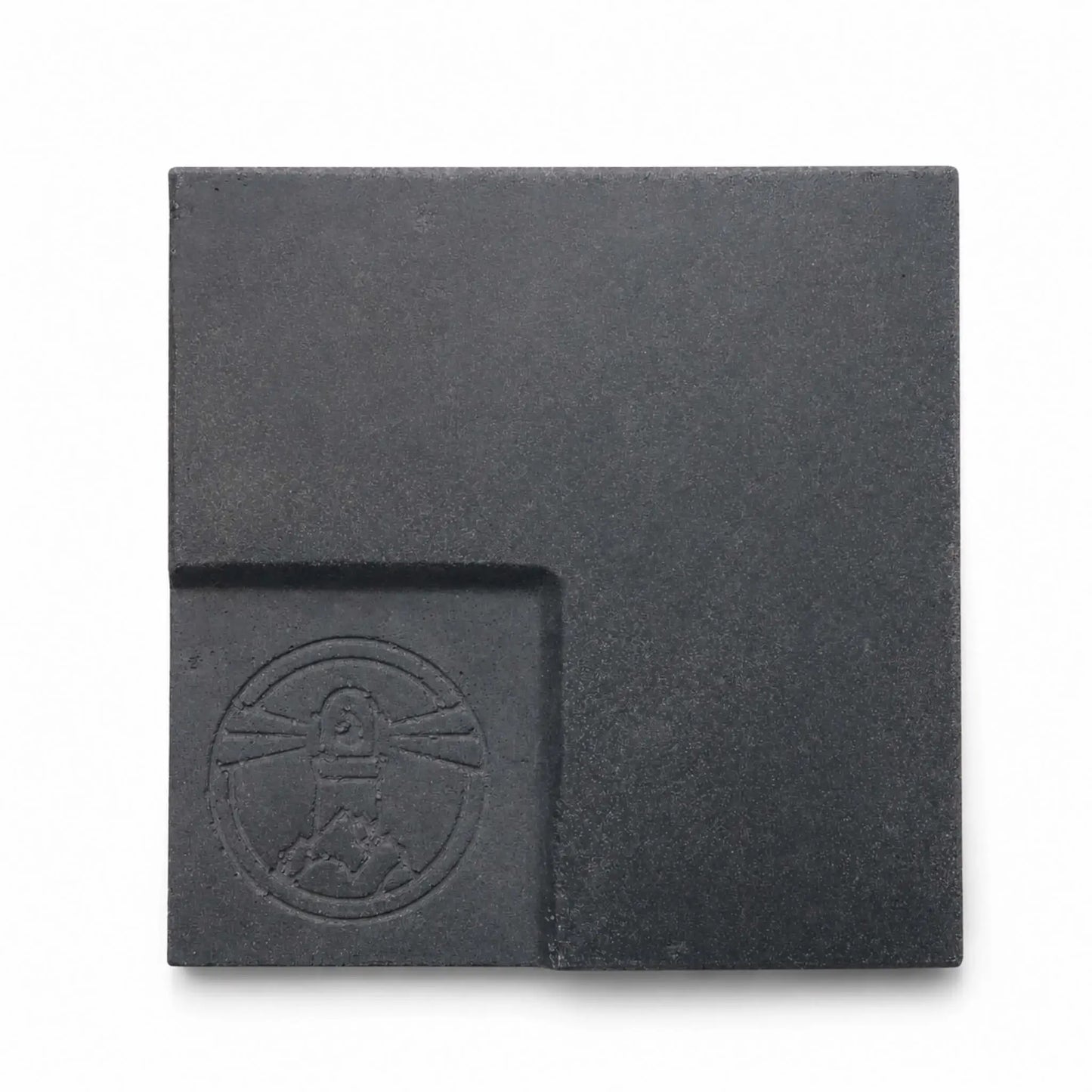 Flame Havens Refuge and Serenity Series GFRC glass fiber reinforced concrete sample in Graphite Black. The square finish swatch has a deep charcoal-black color, fine concrete texture, subtle tonal variation, softly rounded edges, and a recessed lower-left panel featuring an embossed Flame Havens emblem.
