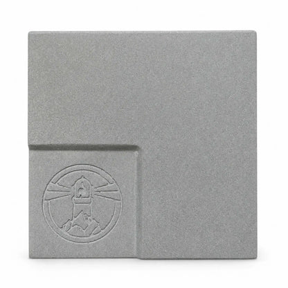 Flame Havens Refuge and Serenity Series GFRC glass fiber reinforced concrete sample in Natural Gray. The square finish swatch shows a medium-gray color with fine concrete texture, soft tonal variation, rounded edges, and a recessed lower-left section featuring an embossed Flame Havens emblem.