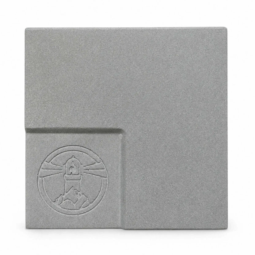 Flame Havens Refuge and Serenity Series GFRC glass fiber reinforced concrete sample in Natural Gray. The square finish swatch shows a medium-gray color with fine concrete texture, soft tonal variation, rounded edges, and a recessed lower-left section featuring an embossed Flame Havens emblem.