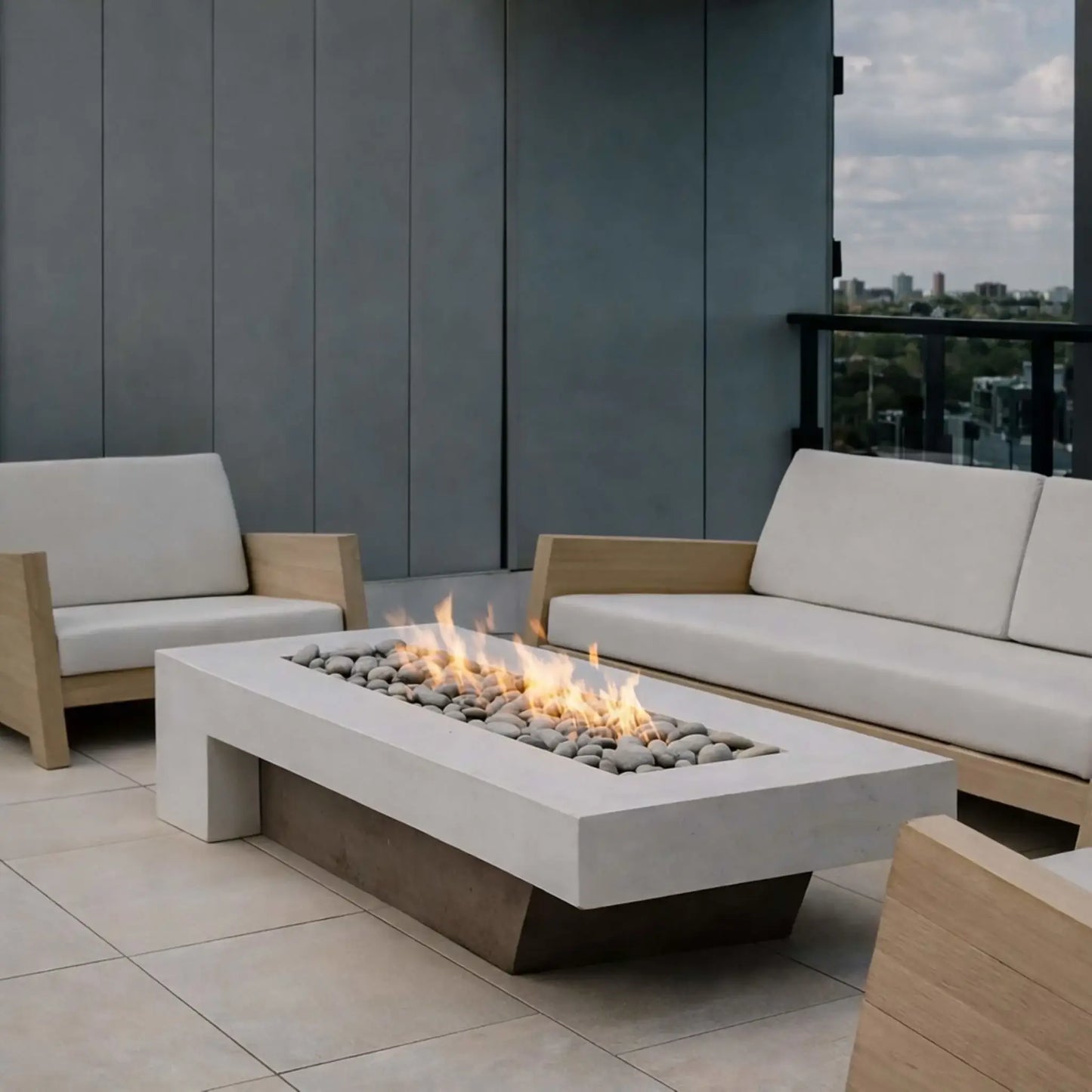 A stylish outdoor lounge area with a rectangular concrete fire pit at the center, surrounded by cushioned seating and poolside lounge chairs. The linear flame glows across dark fire media, complementing the modern architecture and open-air entertaining space.