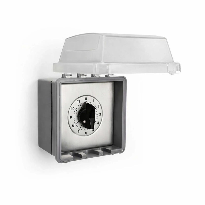 Outdoor-rated timer control housed in a gray weatherproof NEMA enclosure with the protective clear lid flipped open. Inside, a stainless steel timer plate with a 12-hour rotary dial is visible, designed for safe use in exterior environments like fire pits, patios, and commercial installations.