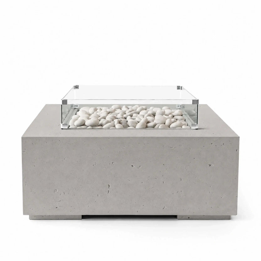 HPC Fire Hearth Products Controls Dekko GFRC Concrete Alea 40 x 40 Fire Pit in Sandstone finish with ivory fire stones filling the recessed burner area. The warm beige concrete body is paired with a clear tempered glass wind guard that frames the decorative media while preserving visibility. Product image highlighting the contemporary square design, durable GFRC construction, and upscale outdoor living appeal.