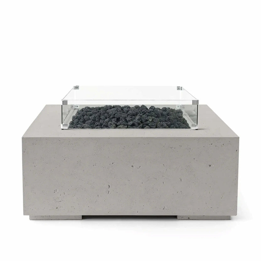 HPC Fire Hearth Products Controls Dekko GFRC Concrete Alea 40 x 40 Fire Pit finished in Sandstone with black lava rock fire media. The square outdoor fire pit features a textured GFRC concrete base and a clear tempered glass wind guard that surrounds the burner area. Professional studio image emphasizing the contrast between the warm sandstone finish and rugged volcanic rock for modern patio installations.