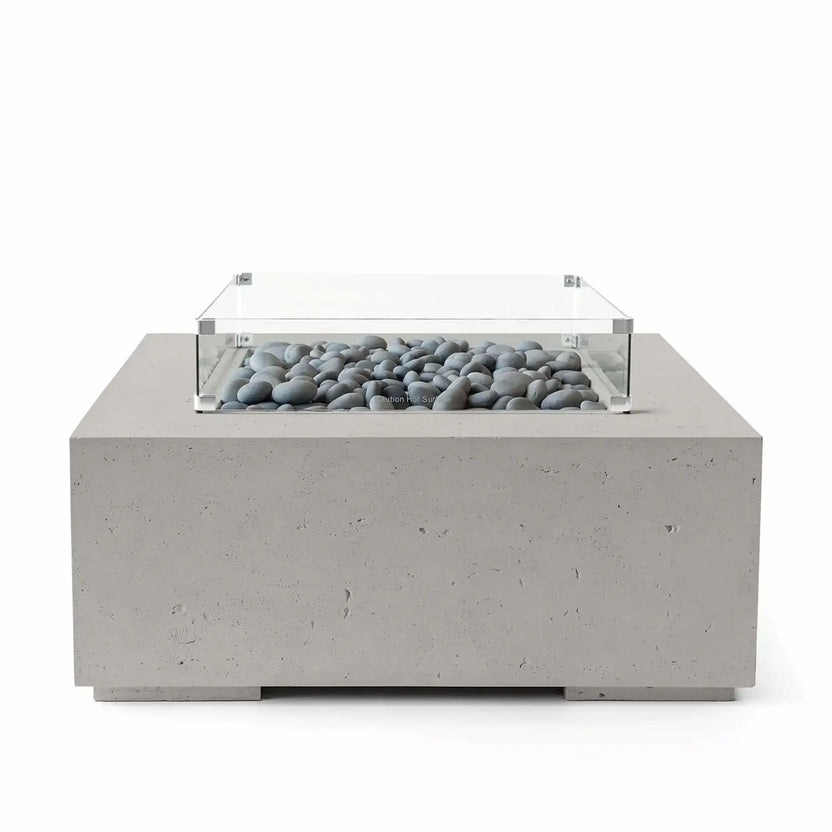 HPC Fire Hearth Products Controls Dekko GFRC Concrete Alea 40 x 40 Fire Pit in Sandstone finish featuring smooth slate stone media beneath a tempered glass wind guard. The warm-toned square GFRC concrete fire pit offers a clean, minimalist appearance with subtle texture and durable construction. Front-facing product image designed to showcase the decorative stone media and premium outdoor fire feature styling.