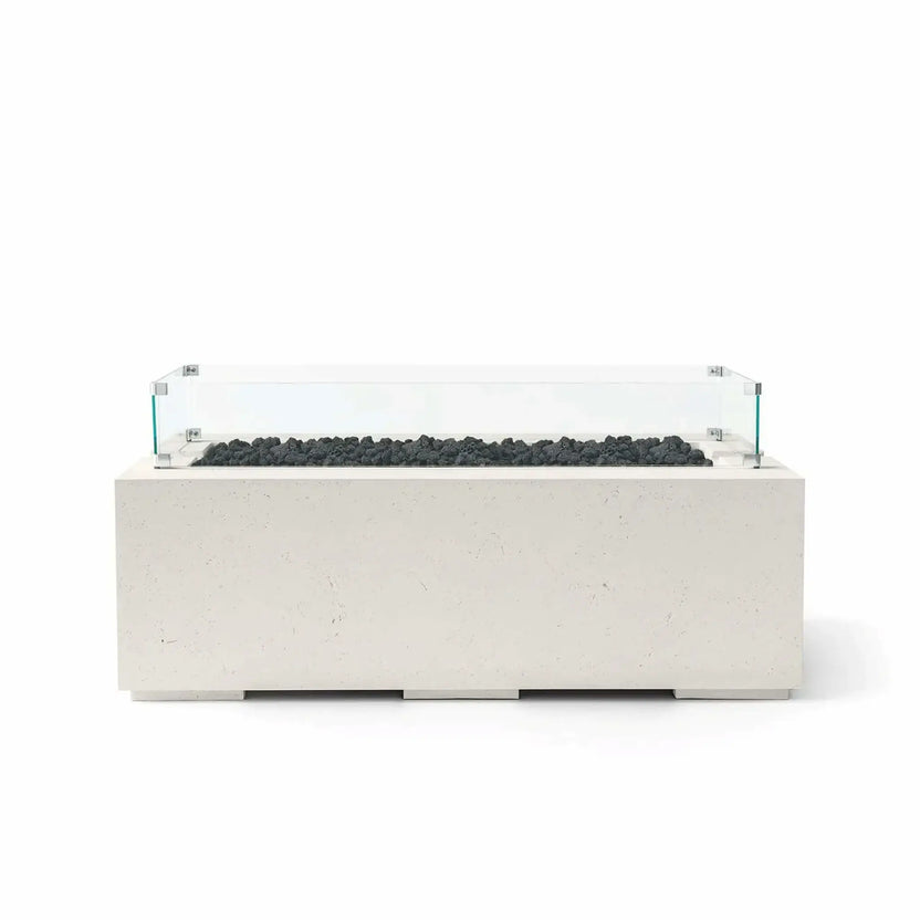 HPC Fire & Hearth Products Dekko GFRC Concrete Avera 48 x 26 Fire Pit in Limestone finish featuring black lava rock fire media and a clear tempered glass wind guard. This modern rectangular outdoor fire pit table showcases a textured GFRC concrete body, linear burner opening, and transparent wind barrier designed to help protect flames while maintaining an elegant, contemporary look for patios, rooftops, poolside seating areas, and outdoor entertaining spaces.