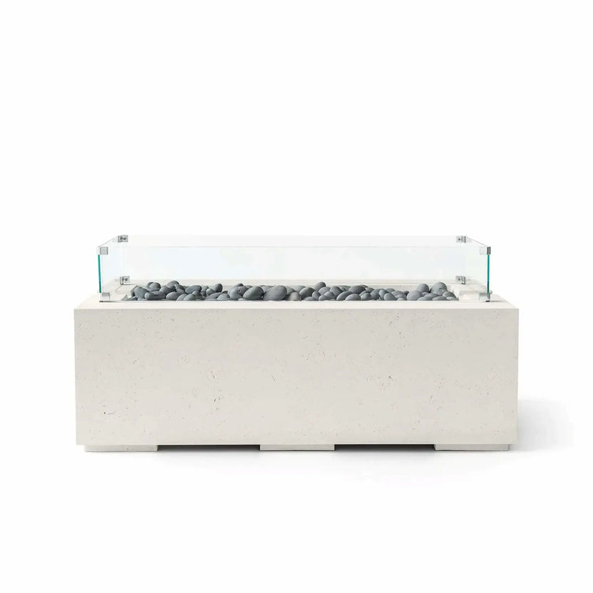 HPC Fire & Hearth Products Dekko GFRC Concrete Avera 48 x 26 Fire Pit Limestone Slate Stone Tempered Glass Wind Guard model shown with smooth gray slate stone media inside a linear burner channel. The limestone-colored GFRC concrete fire table features a low-profile rectangular design and a clear tempered glass wind guard that enhances safety, flame protection, and modern outdoor aesthetics.