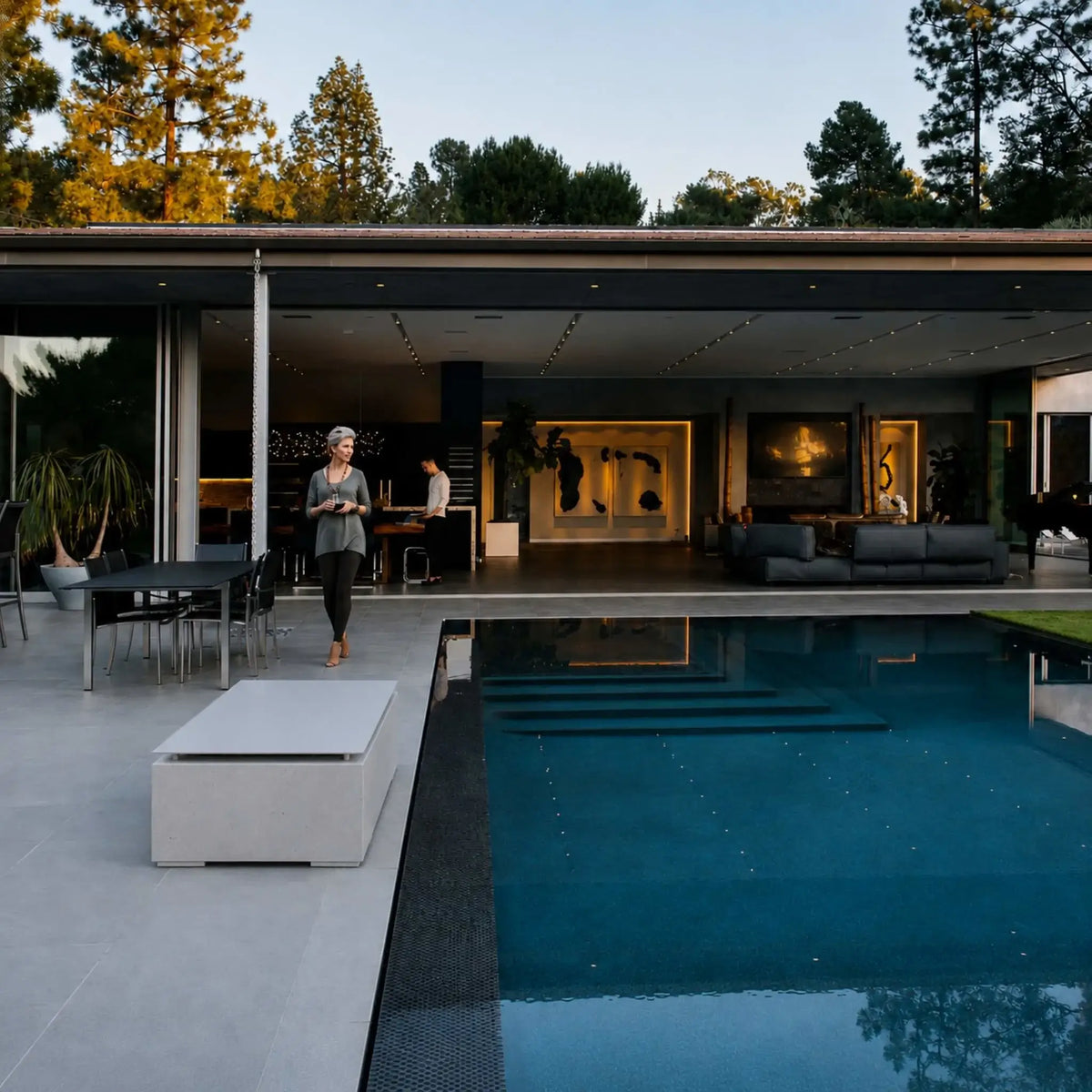 HPC Fire & Hearth Products Dekko GFRC Concrete Avera 48 x 26 Fire Pit Table Top Lid Lifestyle image showing the covered fire pit table positioned beside a luxury swimming pool at a modern contemporary residence. The rectangular concrete fire table with tabletop lid blends seamlessly into the sleek outdoor entertainment space, demonstrating how the protective cover converts the fire feature into a functional surface while maintaining a refined architectural appearance.