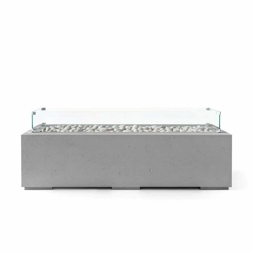 HPC Fire Hearth Products Controls Dekko GFRC Concrete Avera 60 x 26 Fire Pit in Charcoal finish with ivory fire stones and a tempered glass wind guard. The dark gray rectangular concrete fire pit highlights a clean linear burner opening, durable GFRC construction, and contemporary minimalist styling that enhances modern outdoor living areas, patios, and residential landscape designs.