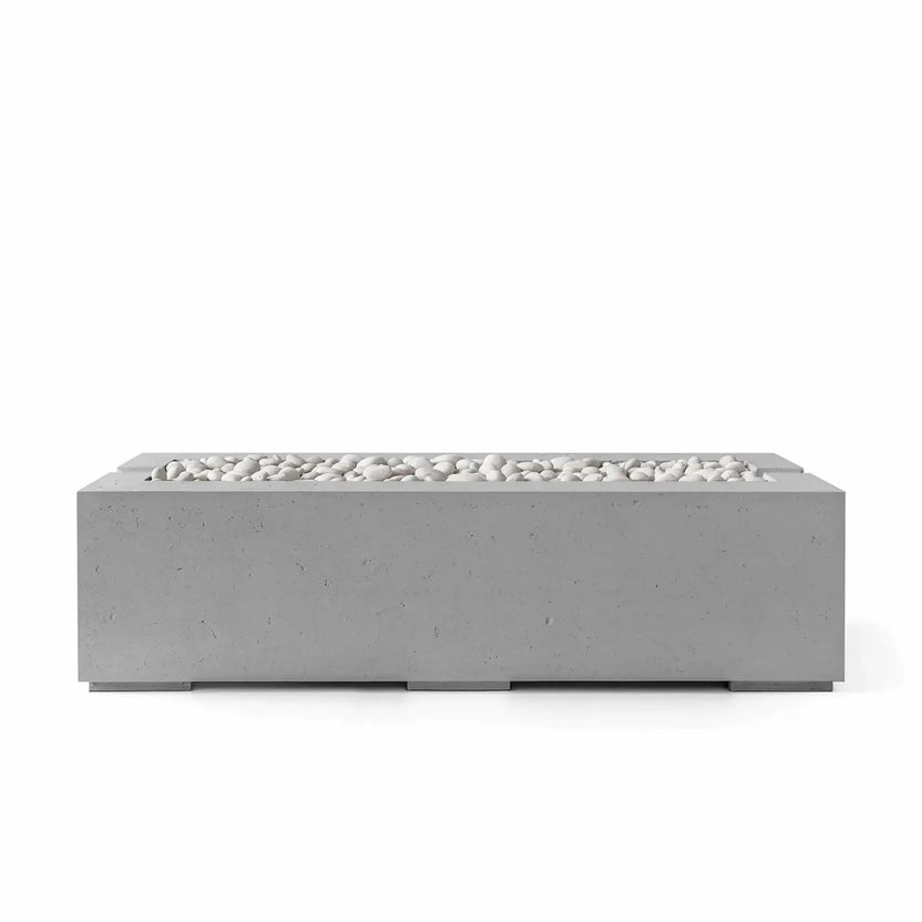 HPC Fire Hearth Products Controls Dekko Avera 60 x 26 GFRC Concrete Fire Pit in Charcoal finish with Ivory Stone media. This modern rectangular gas fire pit features a textured charcoal concrete exterior, recessed linear burner area, and decorative white stones that provide visual contrast for upscale outdoor seating areas, patios, and backyard gathering spaces.