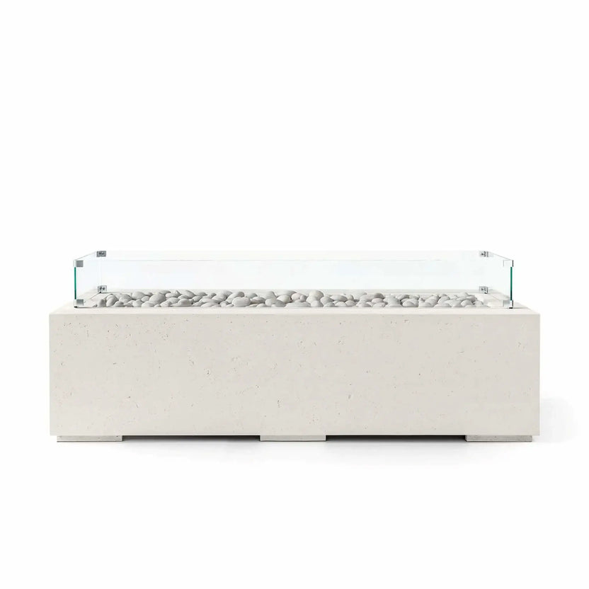 HPC Fire Hearth Products Controls Dekko GFRC Concrete Avera 60 x 26 Fire Pit in Limestone finish featuring ivory fire stones and a tempered glass wind guard around the linear burner. The light-colored rectangular GFRC concrete fire pit offers clean contemporary styling, durable outdoor construction, and a sophisticated minimalist appearance ideal for luxury patios, outdoor seating areas, and modern backyard designs.