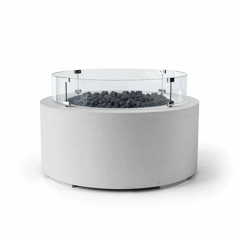 HPC Fire Hearth Products Controls Dekko GFRC Concrete Belmont Fire Pit in Ash finish with Lava Rock media and a Tempered Glass Wind Guard. This round outdoor fire pit features a smooth light gray GFRC concrete body, natural black lava rock fire media, and a circular clear glass windscreen mounted above the burner area. The clean white background highlights the Belmont Fire Pit’s modern aesthetic and functional wind protection.