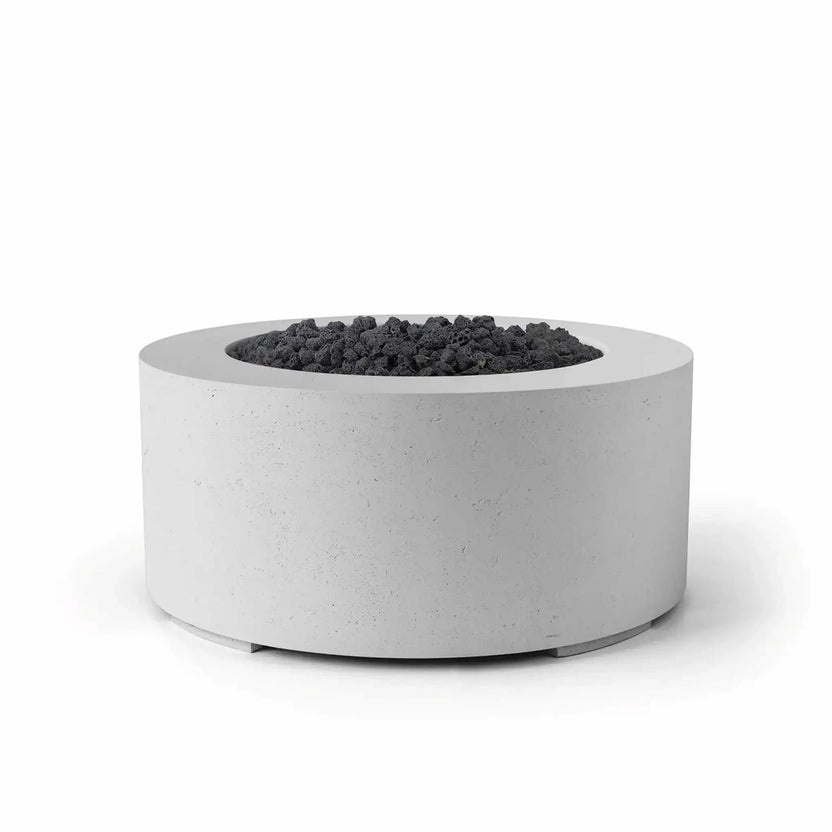 HPC Fire Hearth Products Controls Dekko GFRC Concrete Belmont Fire Pit in Ash finish with black lava rock fire media. This round 36-inch outdoor fire pit features a durable GFRC concrete construction, recessed burner pan, and smooth cylindrical profile. The contrast between the light ash concrete finish and dark lava rock creates a modern, upscale look ideal for patios, backyard gathering areas, resorts, and outdoor entertainment spaces.