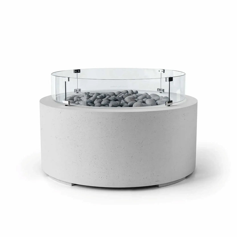 HPC Fire Hearth Products Controls Dekko GFRC Concrete Belmont Fire Pit in Ash finish with Slate Stone fire media and a Tempered Glass Wind Guard. The contemporary round fire pit features a light gray concrete exterior, polished gray slate stones surrounding the burner area, and a transparent circular wind guard supported by stainless steel hardware. Ideal for upscale patios, this Belmont Fire Pit balances style, safety, and performance.
