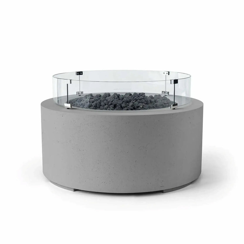 HPC Fire Hearth Products Controls Dekko GFRC Concrete Belmont Fire Pit in Charcoal finish with Lava Rock media and a Tempered Glass Wind Guard. The round GFRC concrete fire pit features a rich charcoal-gray exterior, rugged black lava rock fire media, and a clear glass windscreen secured with metal mounting brackets. This Belmont Fire Pit is designed to enhance outdoor entertaining areas while providing contemporary style and added flame protection.