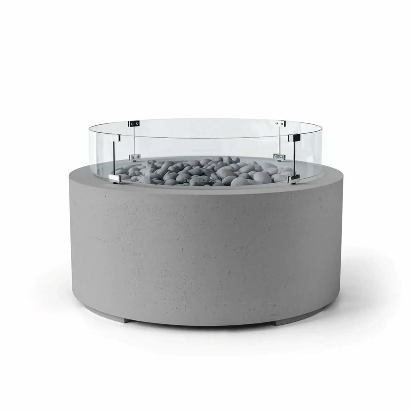 HPC Fire Hearth Products Controls Dekko GFRC Concrete Belmont Fire Pit in Charcoal finish featuring Slate Stone media and a Tempered Glass Wind Guard. This modern outdoor fire pit combines a cylindrical charcoal concrete base with polished gray slate stones and a circular clear glass windscreen around the burner area. The Belmont Fire Pit offers an elegant architectural look while helping protect flames in open-air environments.