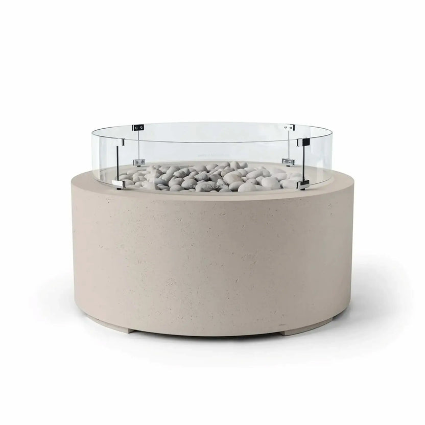 HPC Fire Hearth Products Controls Dekko GFRC Concrete Belmont Fire Pit in Clay finish with Ivory Stone fire media and a Tempered Glass Wind Guard. The warm beige concrete fire pit features a round profile, decorative ivory stones, and a transparent glass windscreen mounted above the burner opening. Shown on a white background, this Belmont Fire Pit blends natural tones with contemporary outdoor design and practical wind protection.