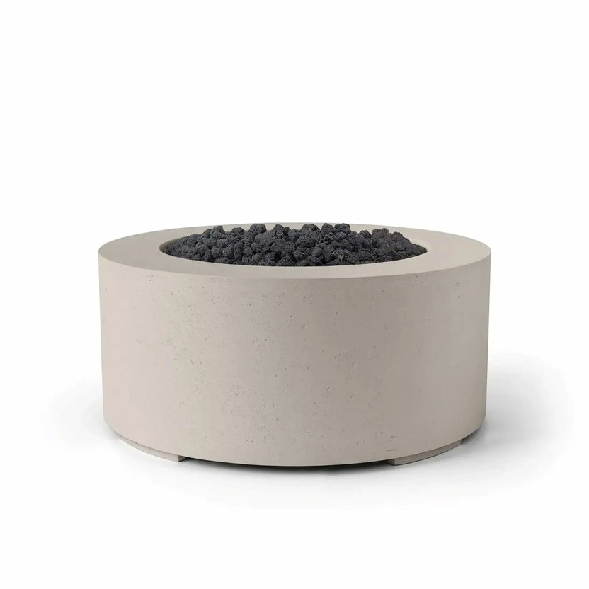 HPC Fire Hearth Products Controls Dekko GFRC Concrete Belmont Fire Pit in Clay finish featuring black lava rock media. The round outdoor gas fire pit combines a warm clay-colored GFRC concrete exterior with rugged dark volcanic rock in the burner area. Its modern low-profile design, textured concrete surface, and clean circular shape create a sophisticated focal point for outdoor entertaining and backyard living spaces.