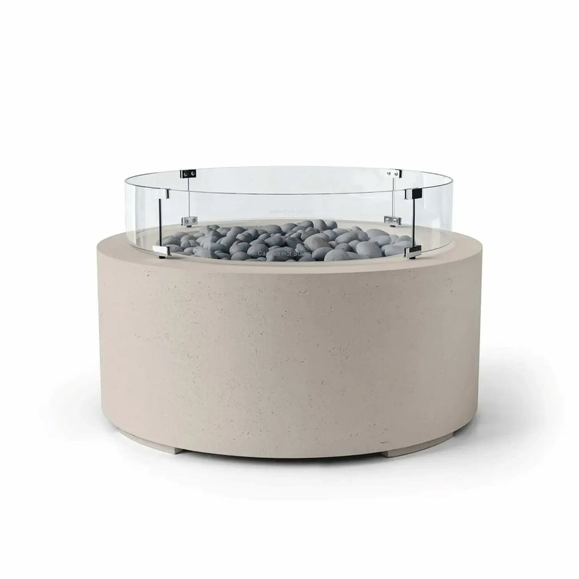 HPC Fire Hearth Products Controls Dekko GFRC Concrete Belmont Fire Pit in Clay finish with Slate Stone media and a Tempered Glass Wind Guard. The fire pit features a warm clay-colored concrete base, smooth gray slate stones around the burner area, and a circular clear glass windscreen secured with stainless steel supports. Displayed on a white background, the Belmont Fire Pit combines refined aesthetics with functional outdoor performance.
