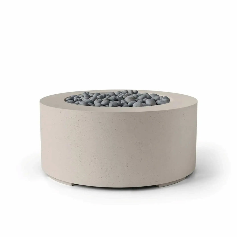 HPC Fire Hearth Products Controls Dekko GFRC Concrete Belmont Fire Pit in Clay finish with slate stone fire media. This contemporary round fire pit showcases durable GFRC concrete construction, a smooth cylindrical silhouette, and a recessed burner area filled with decorative gray stones. The neutral clay finish enhances its modern architectural appearance, making it suitable for upscale residential patios and commercial outdoor environments.