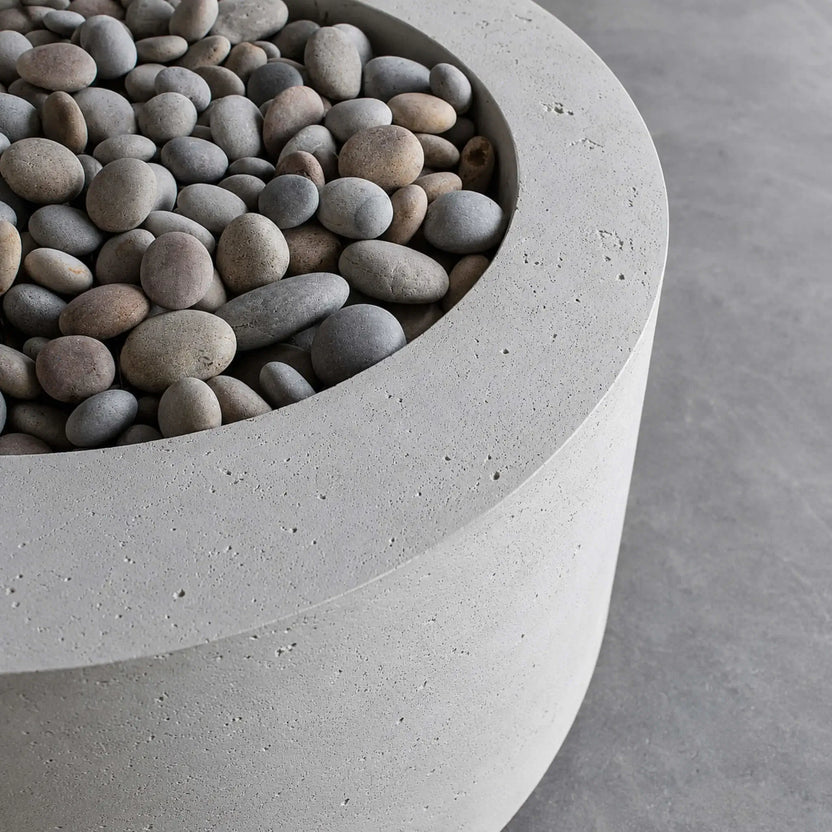 Close-up detail of the HPC Fire Hearth Products Controls Dekko GFRC Concrete Belmont Fire Pit showing the textured concrete rim and recessed fire media area filled with smooth decorative river stones. This lifestyle image highlights the premium GFRC concrete construction, subtle surface texture, rounded edges, and refined craftsmanship that define the Belmont Fire Pit’s modern outdoor design.