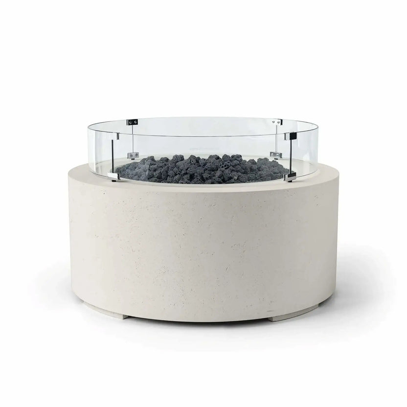 HPC Fire Hearth Products Controls Dekko GFRC Concrete Belmont Fire Pit in Limestone finish with Lava Rock fire media and a Tempered Glass Wind Guard. The round outdoor fire pit features an off-white GFRC concrete base, dark volcanic lava rock surrounding the burner area, and a circular clear glass windscreen secured with stainless steel brackets. Displayed on a clean white background, this Belmont Fire Pit offers a modern, durable centerpiece for upscale patios and outdoor living spaces.