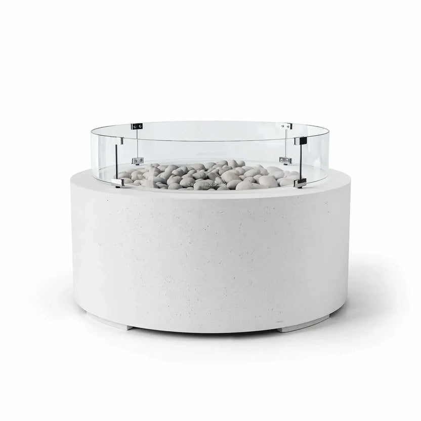 HPC Fire Hearth Products Controls Dekko GFRC Concrete Belmont Fire Pit in Natural finish with Ivory Stone fire media and a Tempered Glass Wind Guard. The fire pit features a bright white GFRC concrete cylindrical base, decorative ivory stones filling the burner area, and a clear round glass windscreen attached with stainless steel brackets. Shown on a white background, this Belmont Fire Pit delivers a clean architectural look for luxury outdoor spaces.