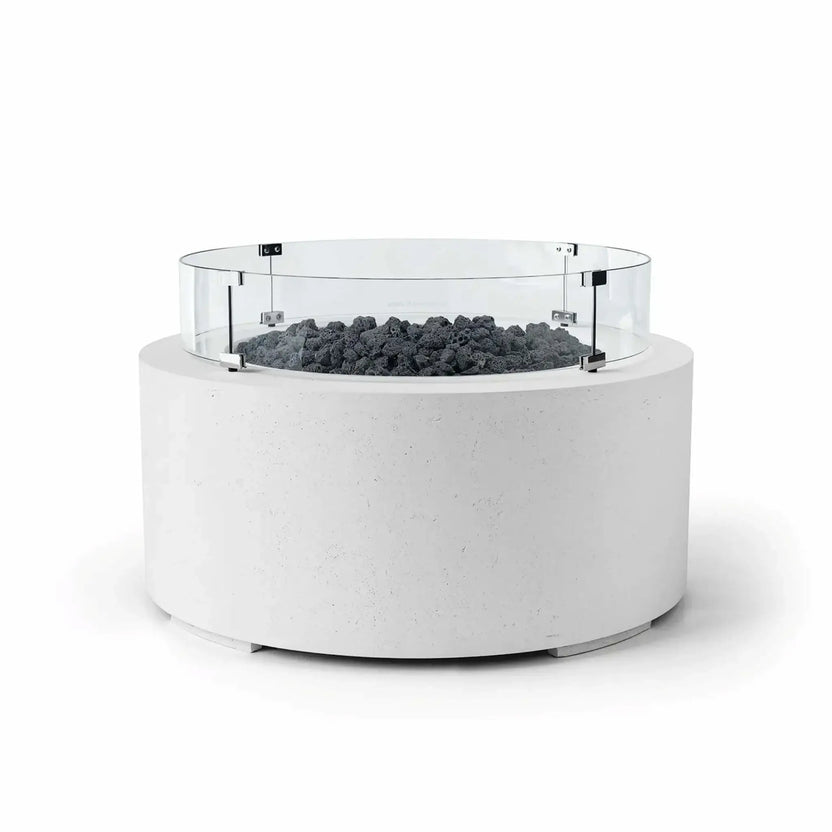 HPC Fire Hearth Products Controls Dekko GFRC Concrete Belmont Fire Pit in Natural finish featuring Lava Rock media and a Tempered Glass Wind Guard. This round outdoor fire pit combines a crisp white GFRC concrete body with rugged black lava rock and a transparent circular glass windscreen for added flame protection. The Belmont Fire Pit’s modern silhouette and contrasting materials create a striking focal point for patios and outdoor gathering areas.