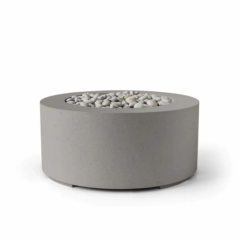 HPC Fire Hearth Products Controls Dekko GFRC Concrete Belmont Fire Pit in Sandstone finish with ivory stone fire media. This contemporary round fire pit features a warm sandstone-gray concrete exterior, durable GFRC construction, and a recessed burner opening filled with smooth decorative ivory stones. Displayed on a white background, the Belmont Fire Pit offers a sophisticated blend of modern design and outdoor functionality for luxury patios and landscape projects.