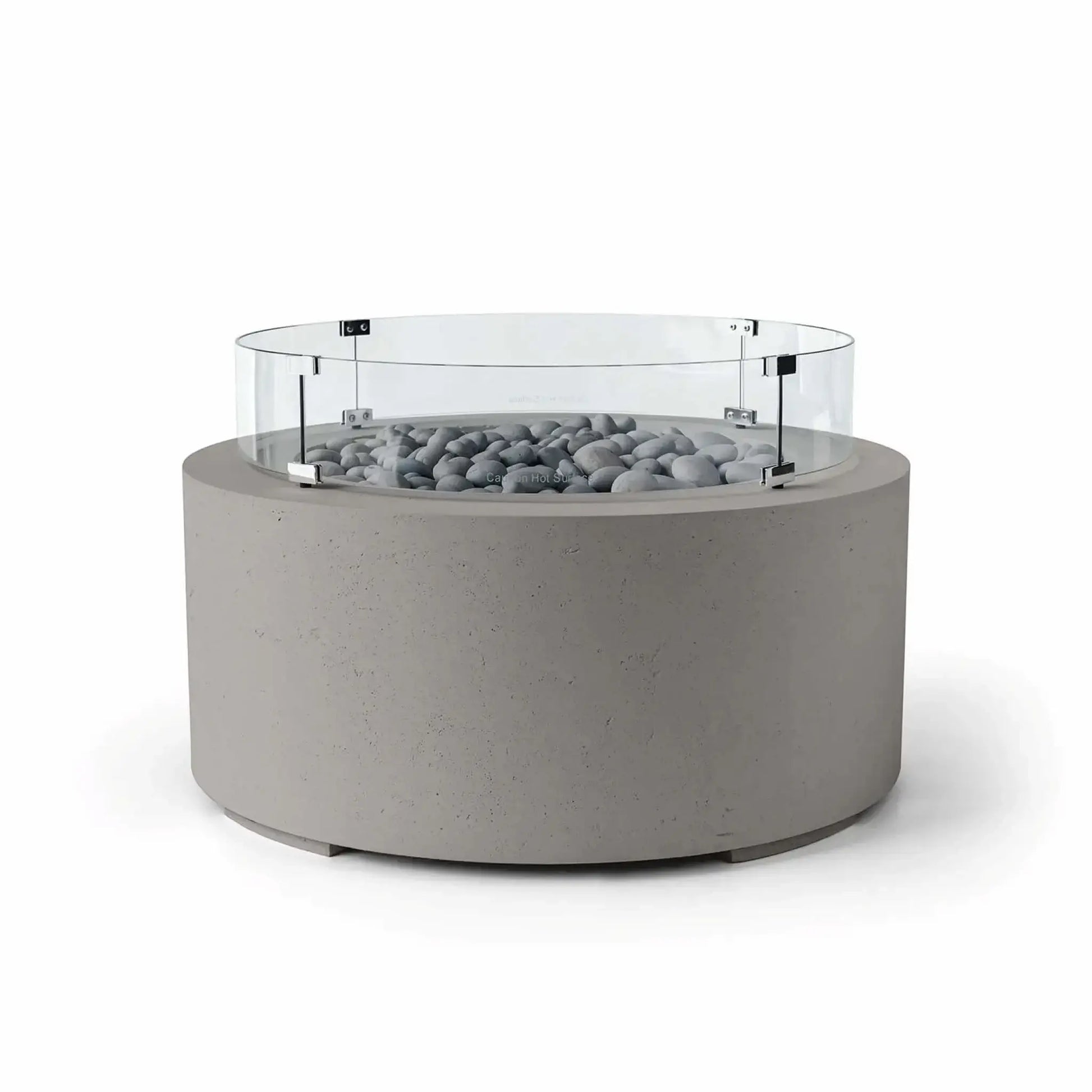 HPC Fire Hearth Products Controls Dekko GFRC Concrete Belmont Fire Pit in Sandstone finish with Slate Stone fire media and a Tempered Glass Wind Guard. This modern round fire pit features a warm beige concrete body, smooth gray slate stones surrounding the burner area, and a clear circular glass windscreen designed for enhanced flame protection. The Belmont Fire Pit serves as an elegant outdoor centerpiece for patios, terraces, and lounge areas.