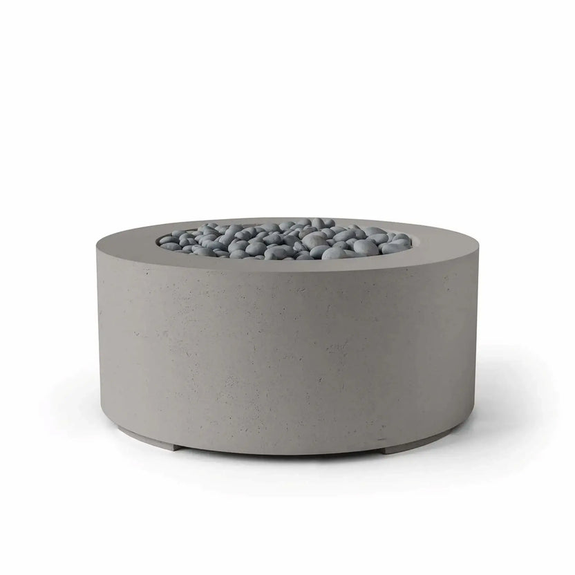 HPC Fire Hearth Products Controls Dekko GFRC Concrete Belmont Fire Pit in Sandstone finish with slate stone fire media. This modern round GFRC concrete fire pit features a neutral sandstone-toned exterior, smooth cylindrical silhouette, and recessed burner area filled with decorative gray slate stones. The Belmont Fire Pit combines clean architectural styling, durable construction, and premium outdoor aesthetics, making it ideal for upscale residential patios and hospitality environments.