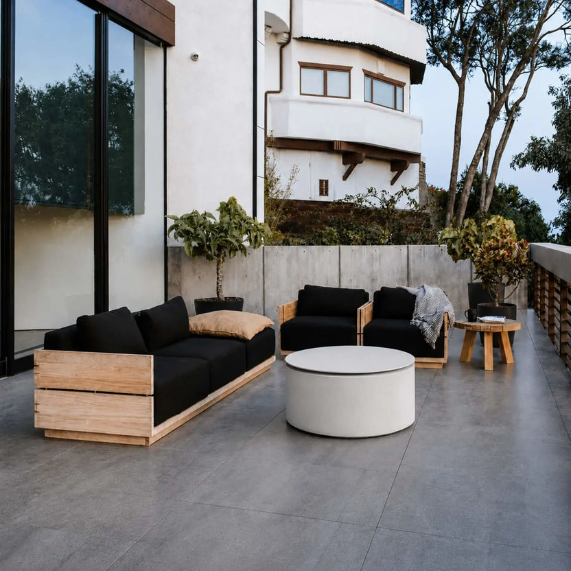 HPC Fire Hearth Products Controls Dekko GFRC Concrete Belmont Fire Pit Table Top Lid featured on a luxury rooftop terrace overlooking a hillside neighborhood. The covered Belmont Fire Pit functions as a modern outdoor coffee table surrounded by contemporary seating, decorative pillows, potted plants, and sleek architectural railings. Warm natural sunlight highlights the clean lines and multifunctional design of this premium outdoor fire pit accessory.