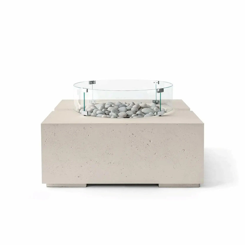 HPC Fire Hearth Products Controls Dekko GFRC Concrete Bravo 32 x 32 Fire Pit in Clay finish featuring Ivory Stone fire media and a tempered glass wind guard. The warm beige concrete tone complements the smooth light-colored stones, creating an elegant modern fire feature with a textured GFRC construction and clean-lined square silhouette.