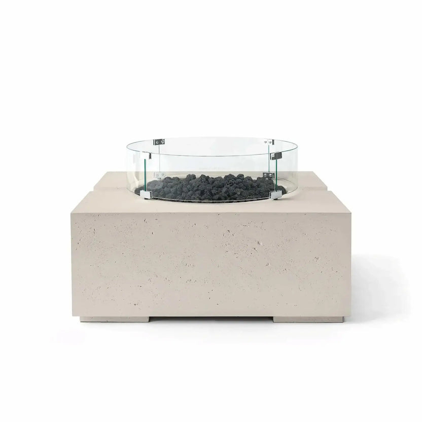 HPC Fire Hearth Products Controls Dekko GFRC Concrete Bravo 32 x 32 Fire Pit in Clay finish with black lava rock fire media and a clear tempered glass wind guard. The warm neutral concrete body contrasts with the dark volcanic rock, highlighting the fire pit’s contemporary outdoor design, textured GFRC construction, and elevated burner platform.