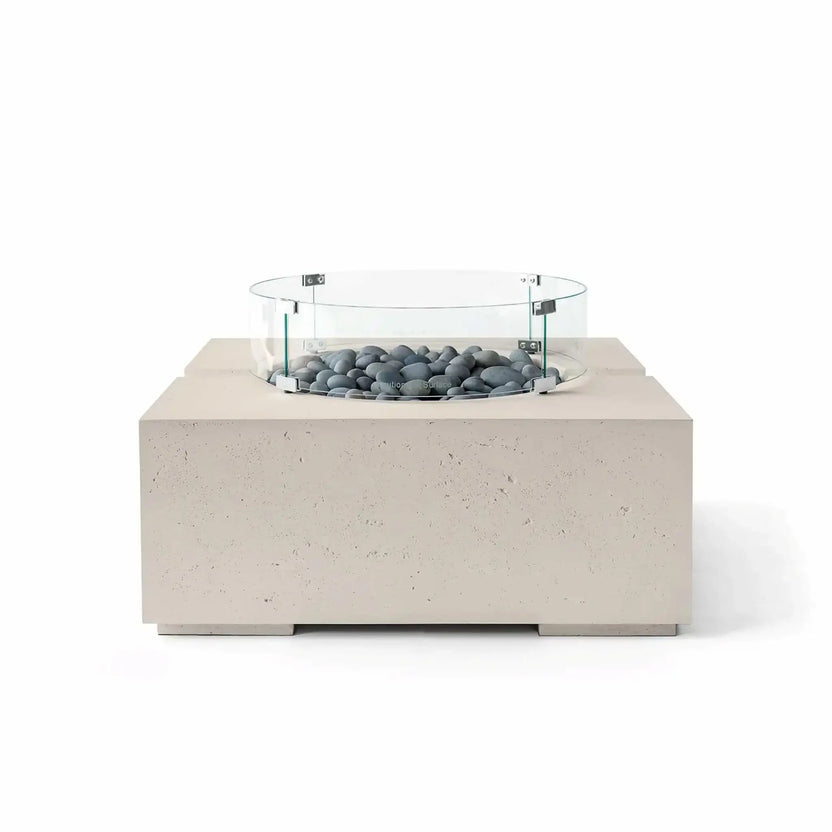 HPC Fire Hearth Products Controls Dekko GFRC Concrete Bravo 32 x 32 Fire Pit in Clay finish featuring Slate Stone fire media and a tempered glass wind guard. This modern square fire pit combines a warm beige textured concrete base with smooth gray decorative stones, offering a refined outdoor gathering centerpiece in a clean studio product image.