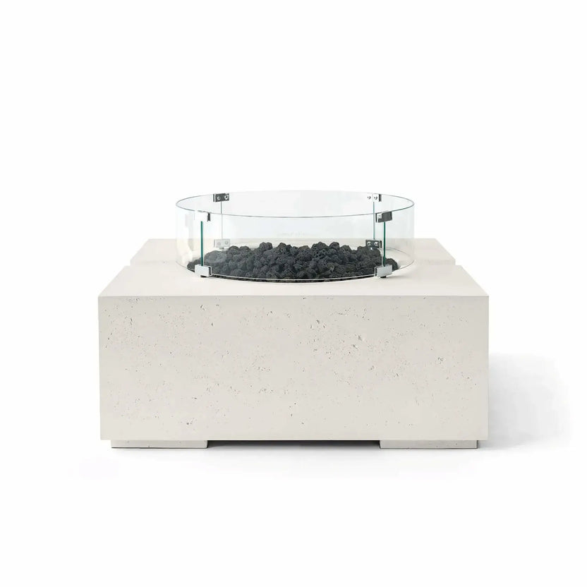 HPC Fire Hearth Products Controls Dekko GFRC Concrete Bravo 32 x 32 Fire Pit in Limestone finish featuring black lava rock fire media and a clear tempered glass wind guard. The light cream-toned GFRC concrete base contrasts with the rugged volcanic rock, creating a modern outdoor fire feature with clean architectural lines, textured detailing, and a raised burner platform, shown in a front-facing studio product image.