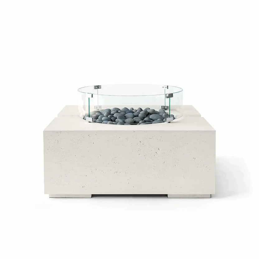HPC Fire Hearth Products Controls Dekko GFRC Concrete Bravo 32 x 32 Fire Pit in Limestone finish with Slate Stone fire media and a tempered glass wind guard. Smooth gray decorative stones complement the light GFRC concrete body, highlighting the fire pit’s contemporary square silhouette, textured finish, and minimalist outdoor design in a clean white-background product photograph.