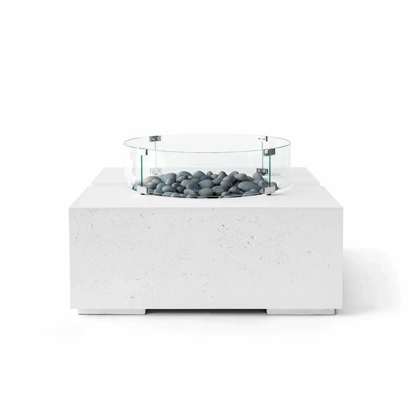 HPC Fire Hearth Products Controls Dekko GFRC Concrete Bravo 32 x 32 Fire Pit in Natural finish featuring Slate Stone fire media and a tempered glass wind guard. The smooth gray stones and bright white concrete base create a sophisticated modern appearance, while the raised burner section and circular glass guard add visual depth and functionality.